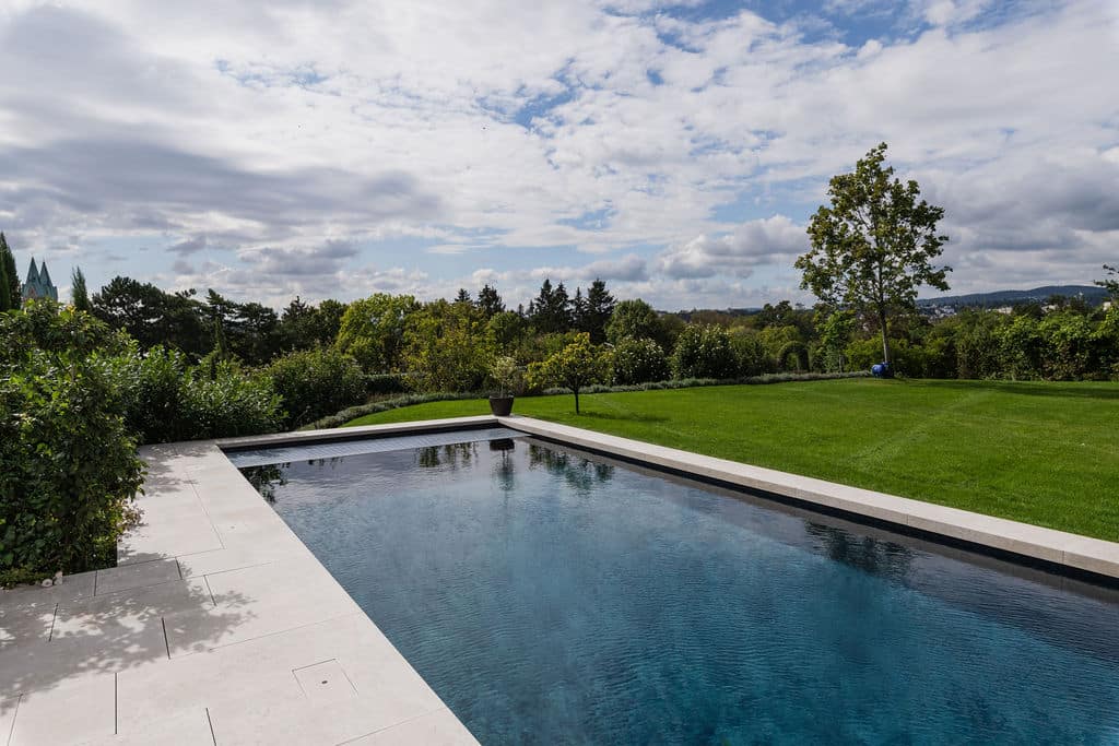 Terrasse und Poolbereich sind mit feinstem San Luca verkleidet. Der warm anmutende Kalkstein aus Kalabrien legt sich mit ruhiger Selbstverständlichkeit in den großzügig angelegten Garten.